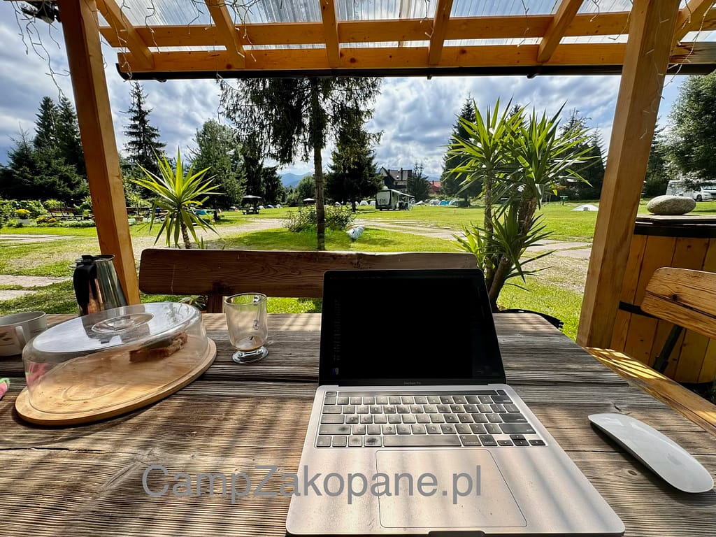 Stanowisko do pracy z laptopem z widokiem na pole kempingowe Camping Harenda w Zakopanem i Tatry w tle.