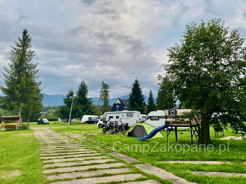 Utwardzona droga przez camping i zielona część z kamperami, namiotem i zjeżdżalnią na Camping Harenda w Zakopanem