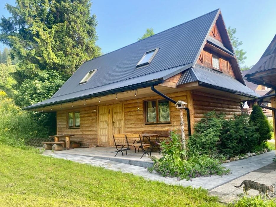 Letni widok domku z bali z tarasem ze stołem i krzesłami w zieleni – Camp Harenda Zakopane